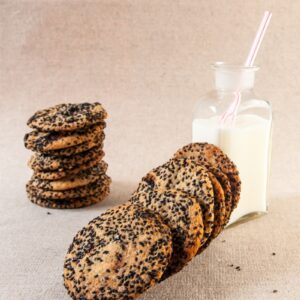 Salty Sesame and Dark Chocolate Chip Cookies stacked next to glass of milk