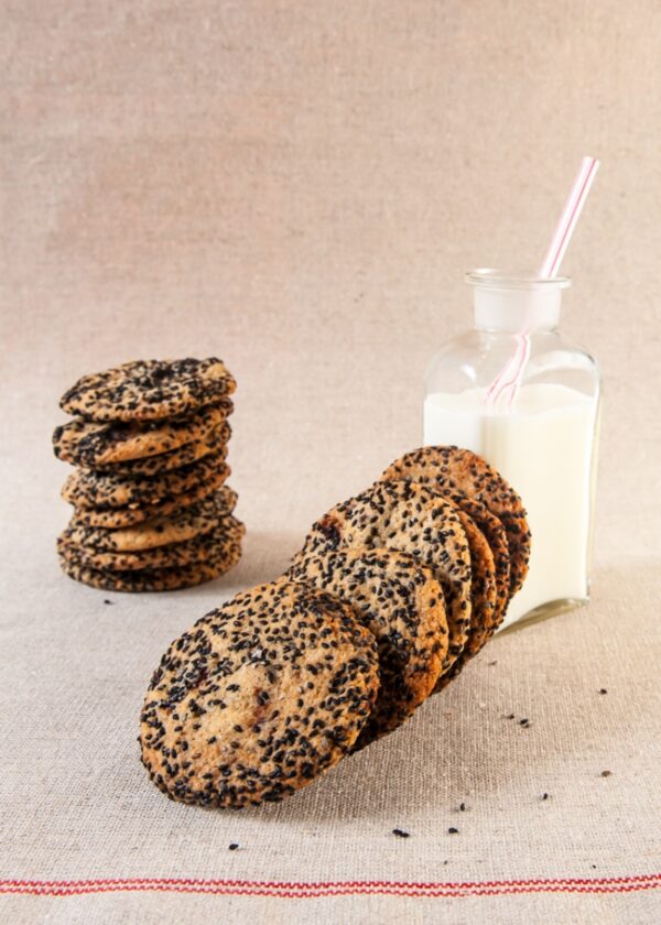 Salty Sesame and Dark Chocolate Chip Cookies stacked next to glass of milk