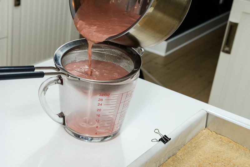 Pouring the cooked cranberry curd through a strainer.