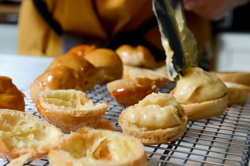 Spooning the pastry cream into the opened pâte-à-choux.