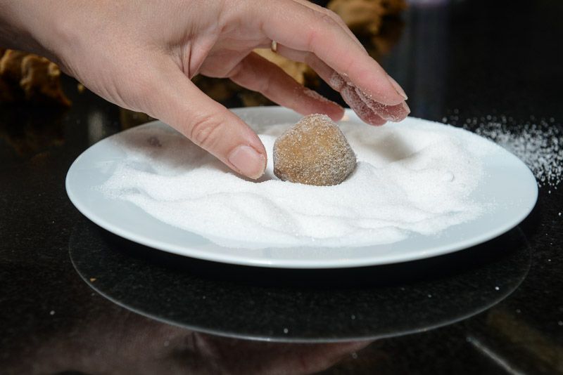 Rolling the cookies in granulated sugar.