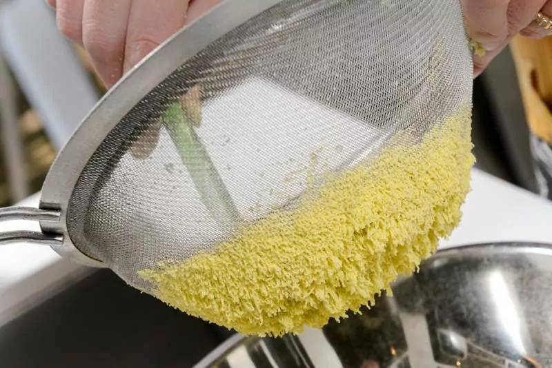 Pushing the cooked egg yolk through a fine sieve.