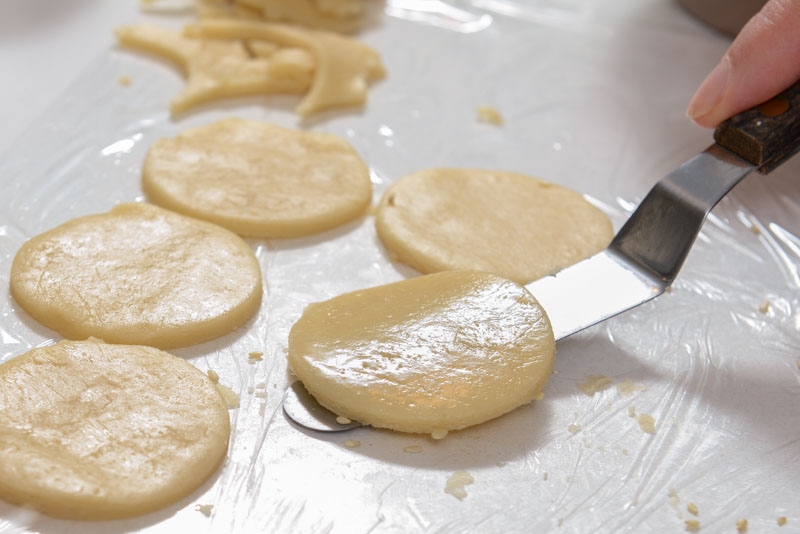 Cookie dough cut into 2 inch rounds. One is brushed with water.