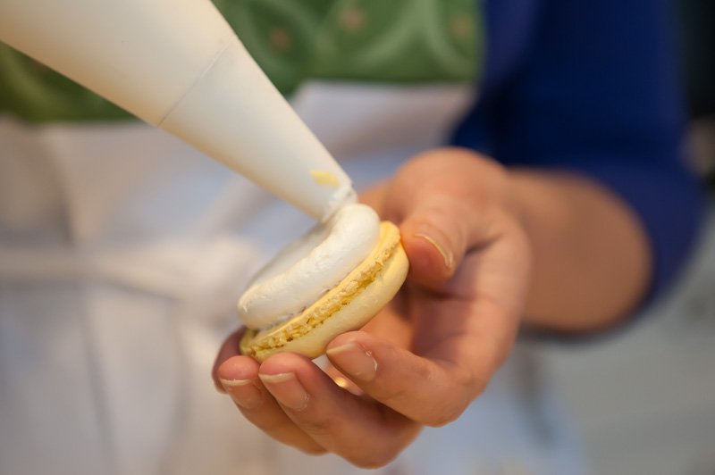 Piping the lemon buttercream onto the macaron half.