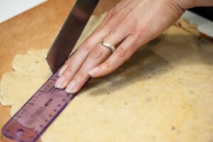 Cutting strips of dough the width of the ruler.