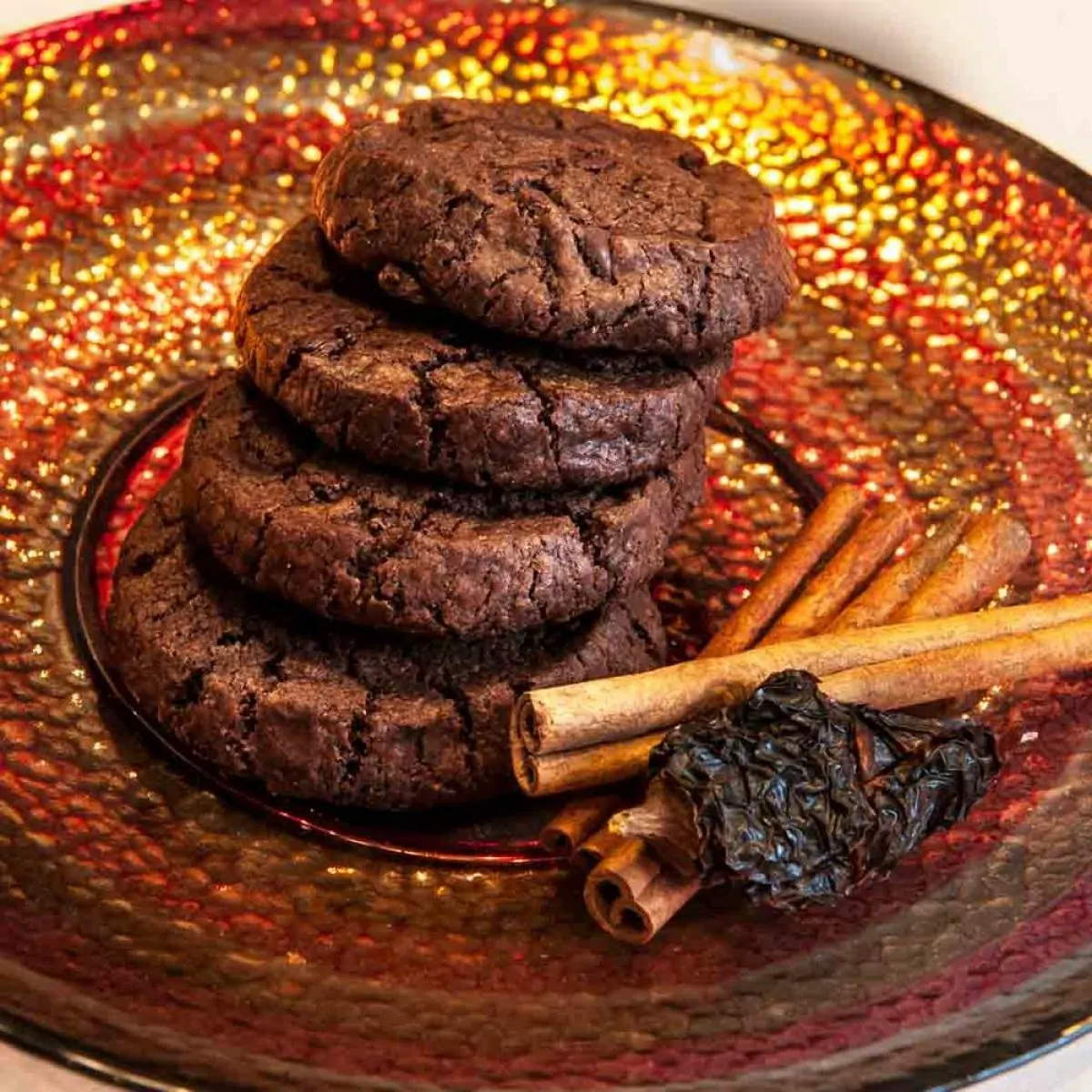 Molé Cookies stacked on decorative plate with cinnamon sticks and chipotle pepper