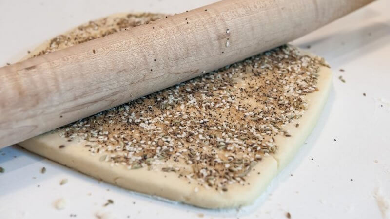 Rolling the seed mixture on the dough.