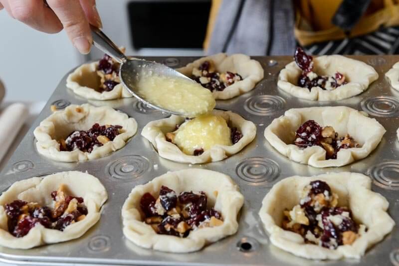 Filling the tartlets with nuts, fruit, eggs, and butter.