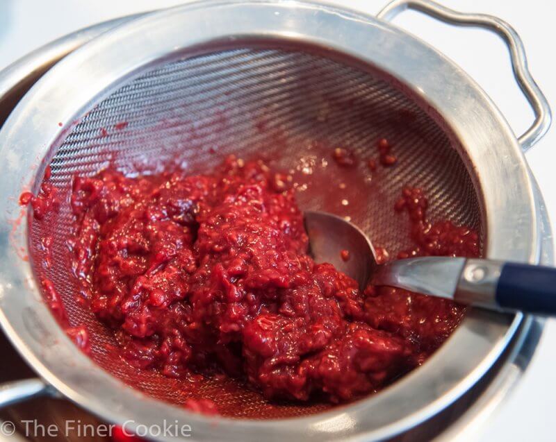 Pushing the frozen then thawed raspberry pulp through the sieve, leaving behind the seeds.